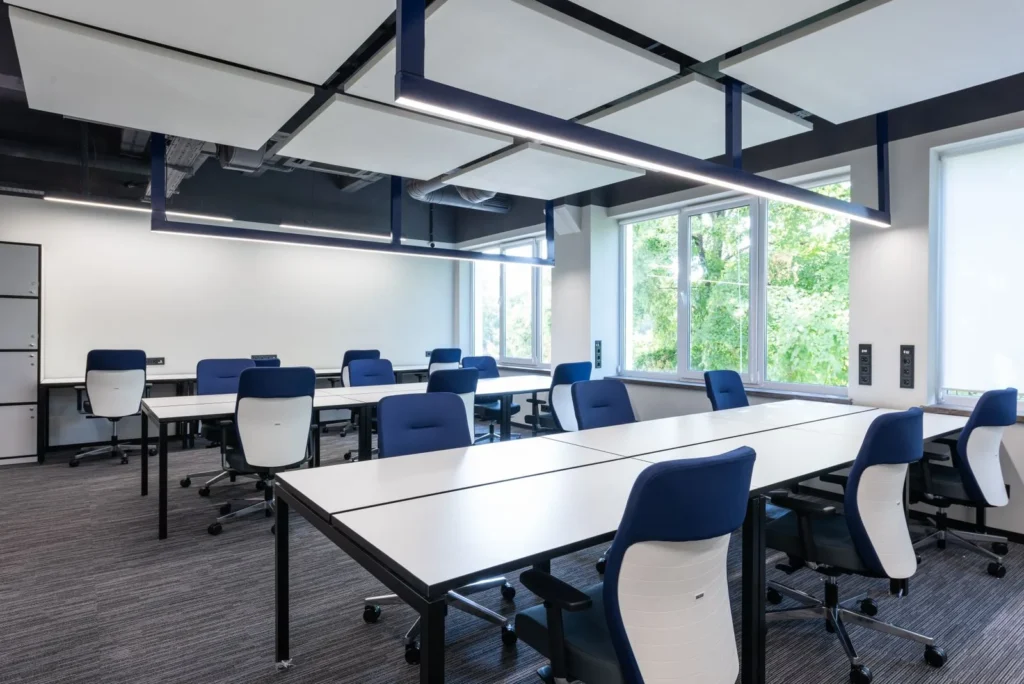 Open plan office with long white desks, blue task chairs and suspended acoustic ceiling panels, an example of commercial space design