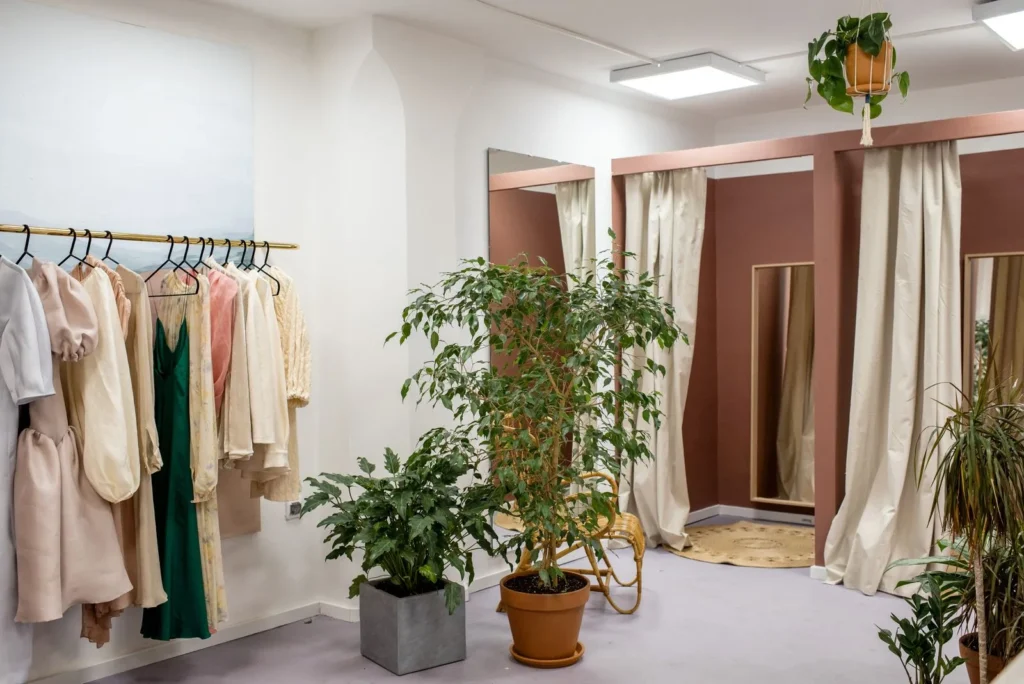 Boutique interior with garments on a brass rail, potted plants and curtained fitting rooms in terracotta tones