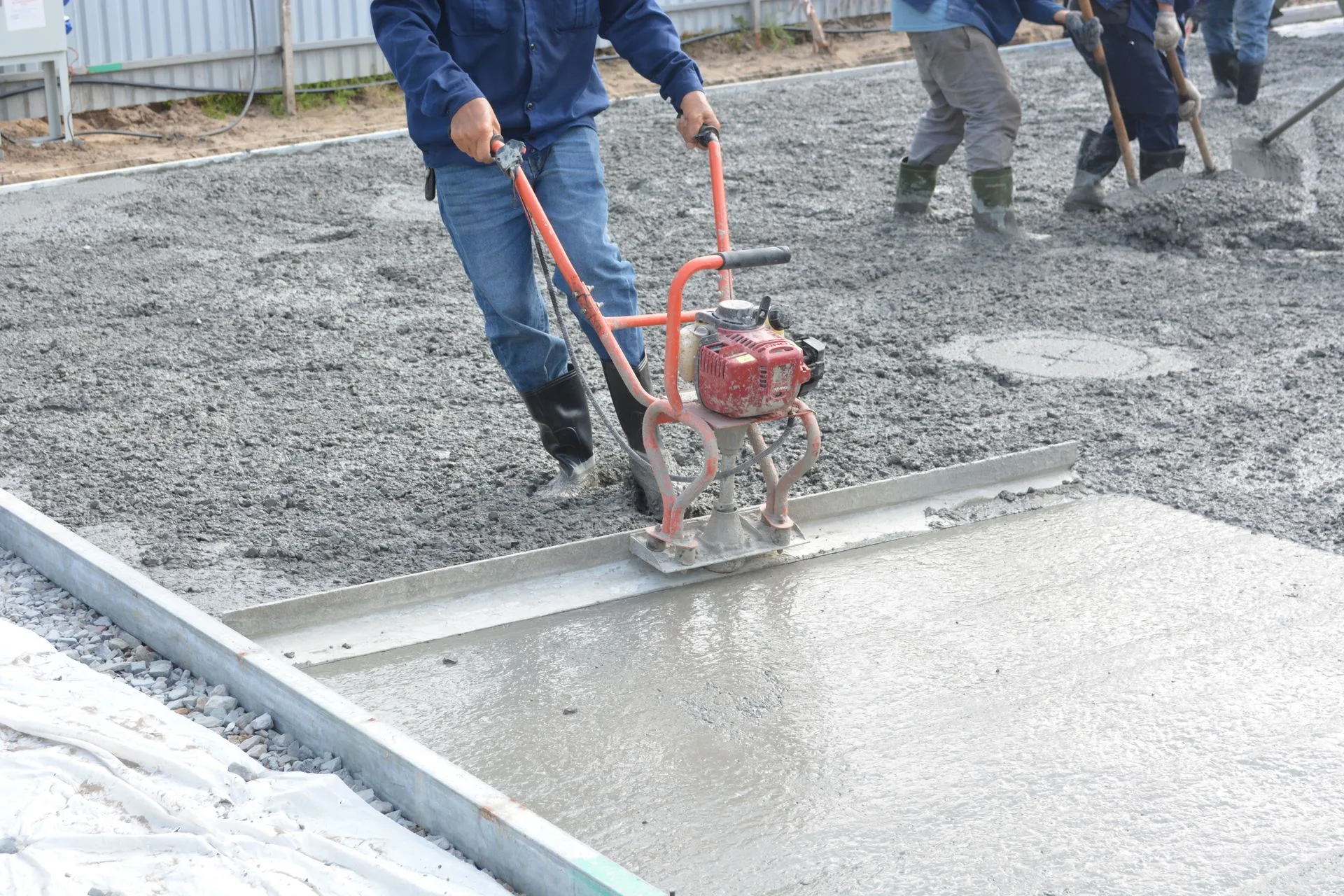 Worker running a power screed over freshly placed concrete laid on a compacted gravel base