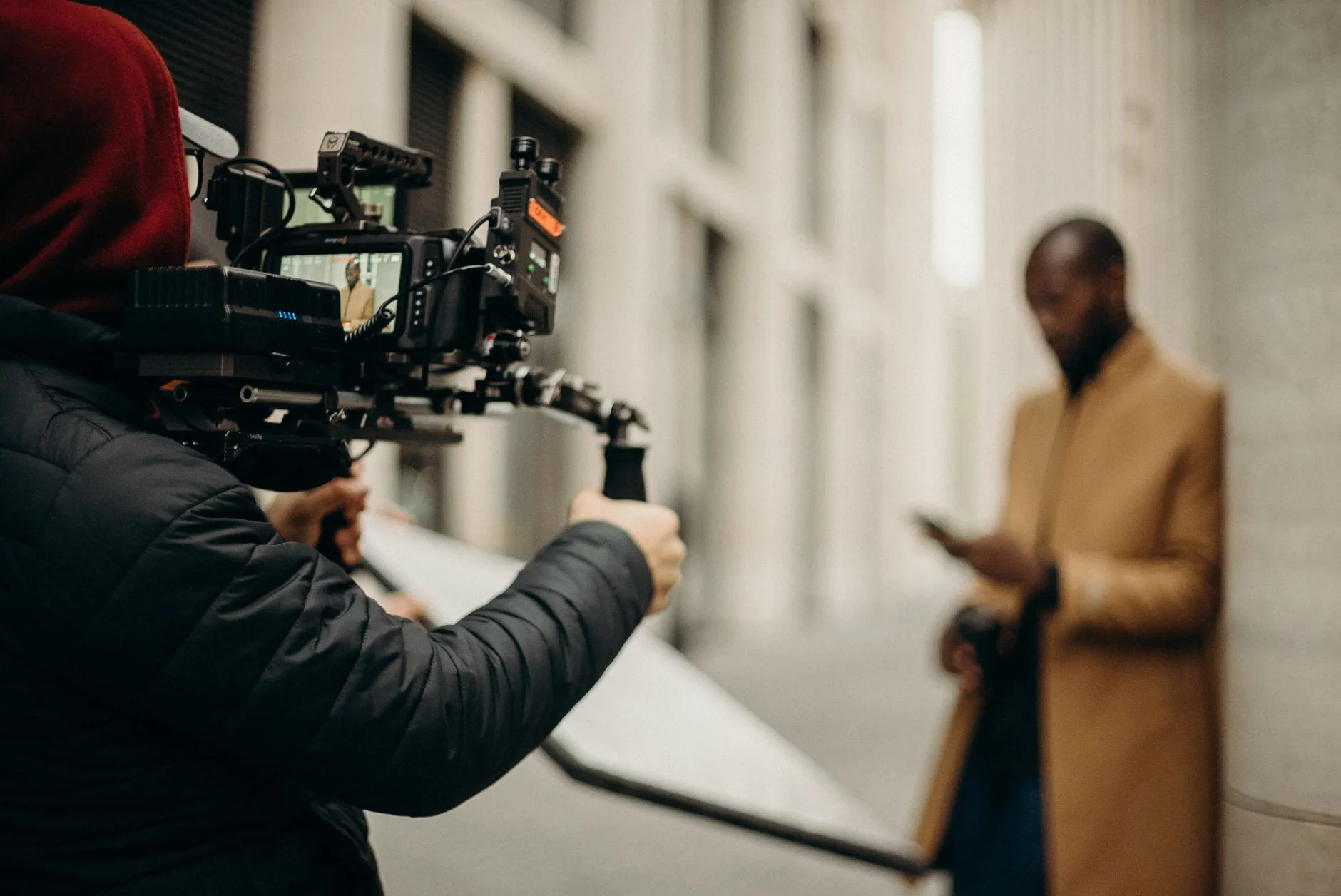 Camera operator filming a man in a camel coat on a city street with a rig-mounted cinema camera