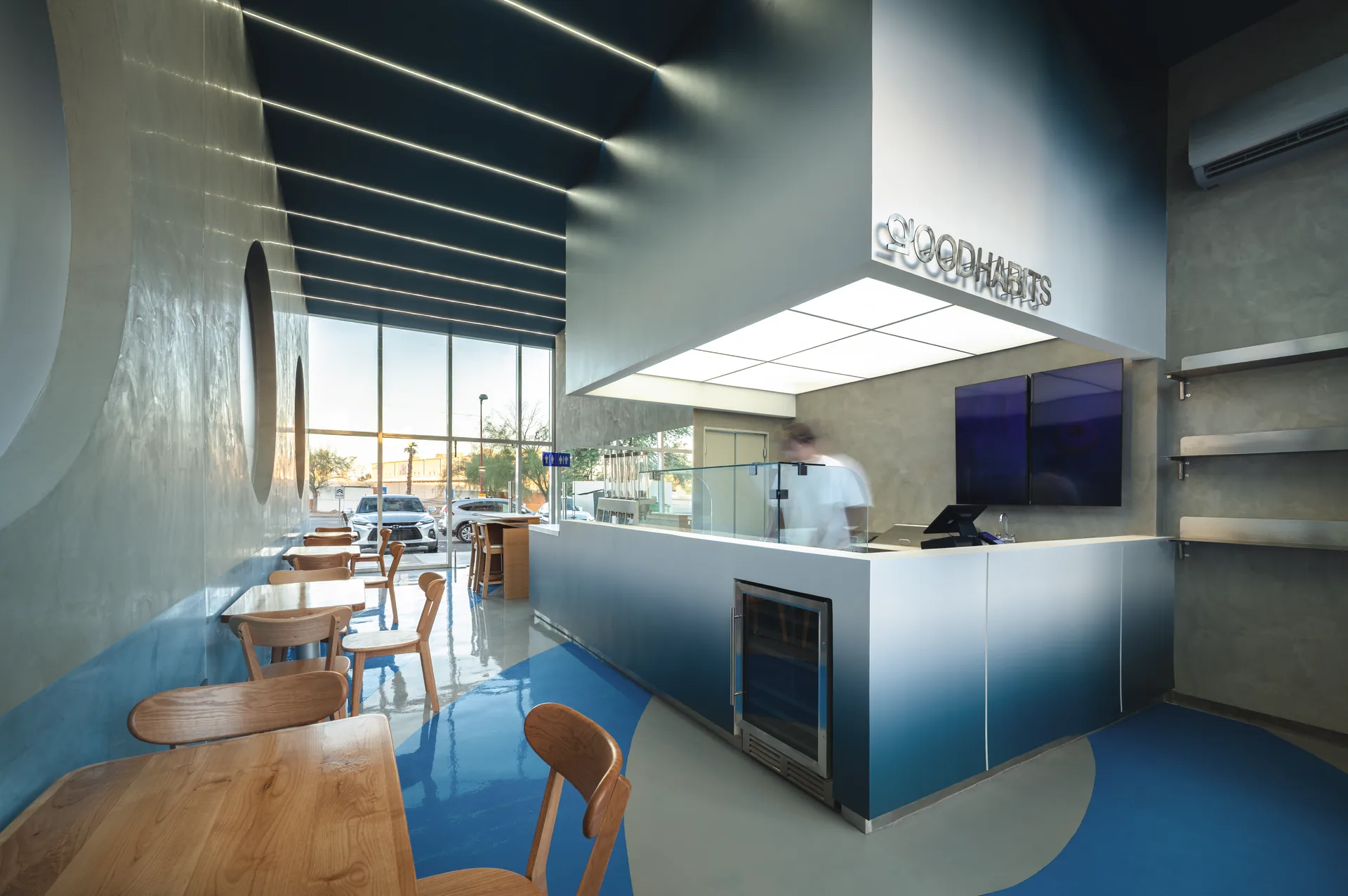 Gradient blue service counter under a suspended white volume with Goodhabits lettering beside a glazed street front