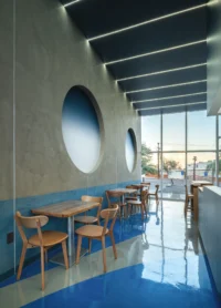 Oak dining tables along a plaster wall with circular niches facing a tall glass storefront
