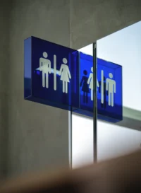 Blue acrylic restroom sign reflected in a glass partition
