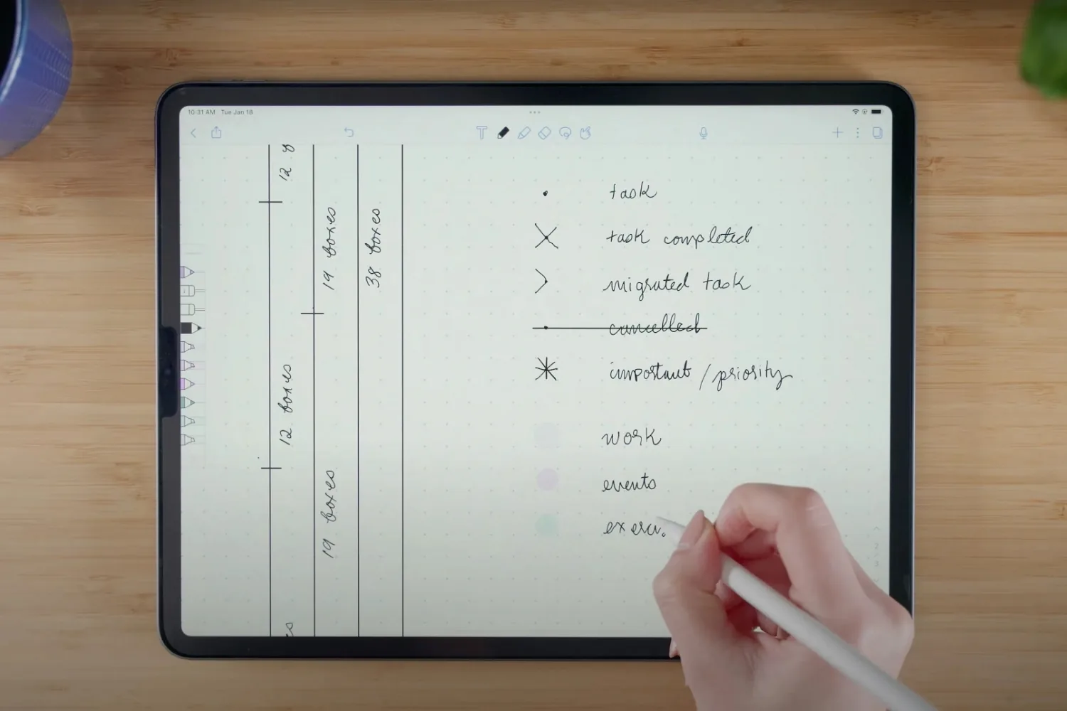 Hand writing a bullet journal key with an Apple Pencil on a lined iPad note