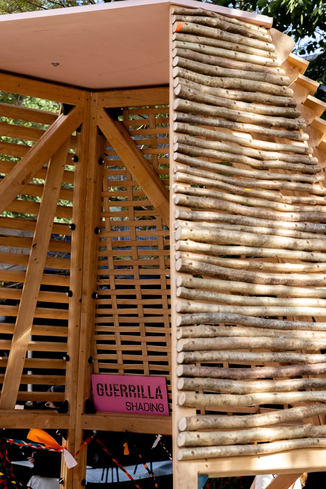 Close view of reused timber slats stacked into a sloping wall of the pavilion with a Guerrilla Shading sign