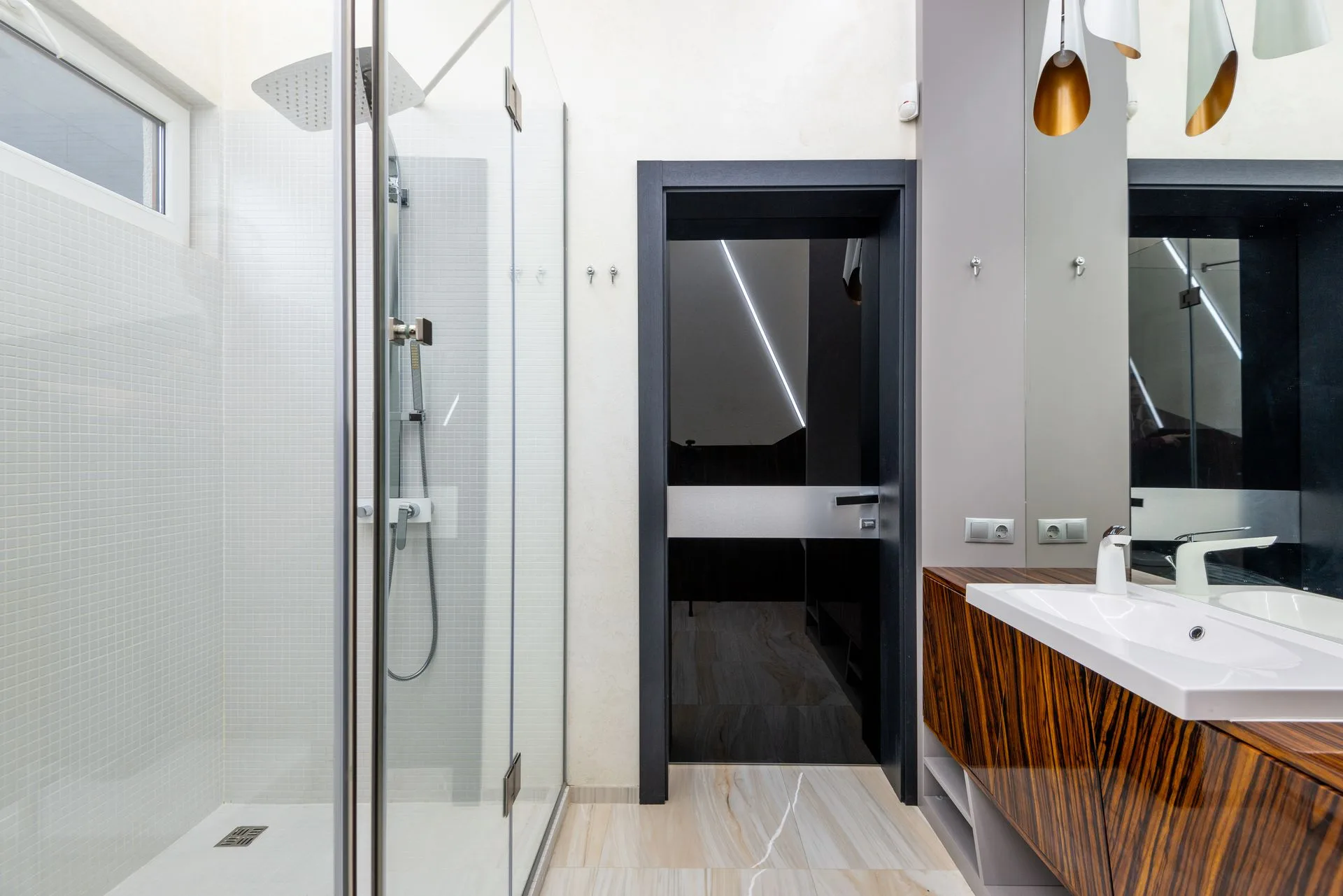 Hinged glass shower door with metal hinges and a rain shower head next to a vanity with a timber front