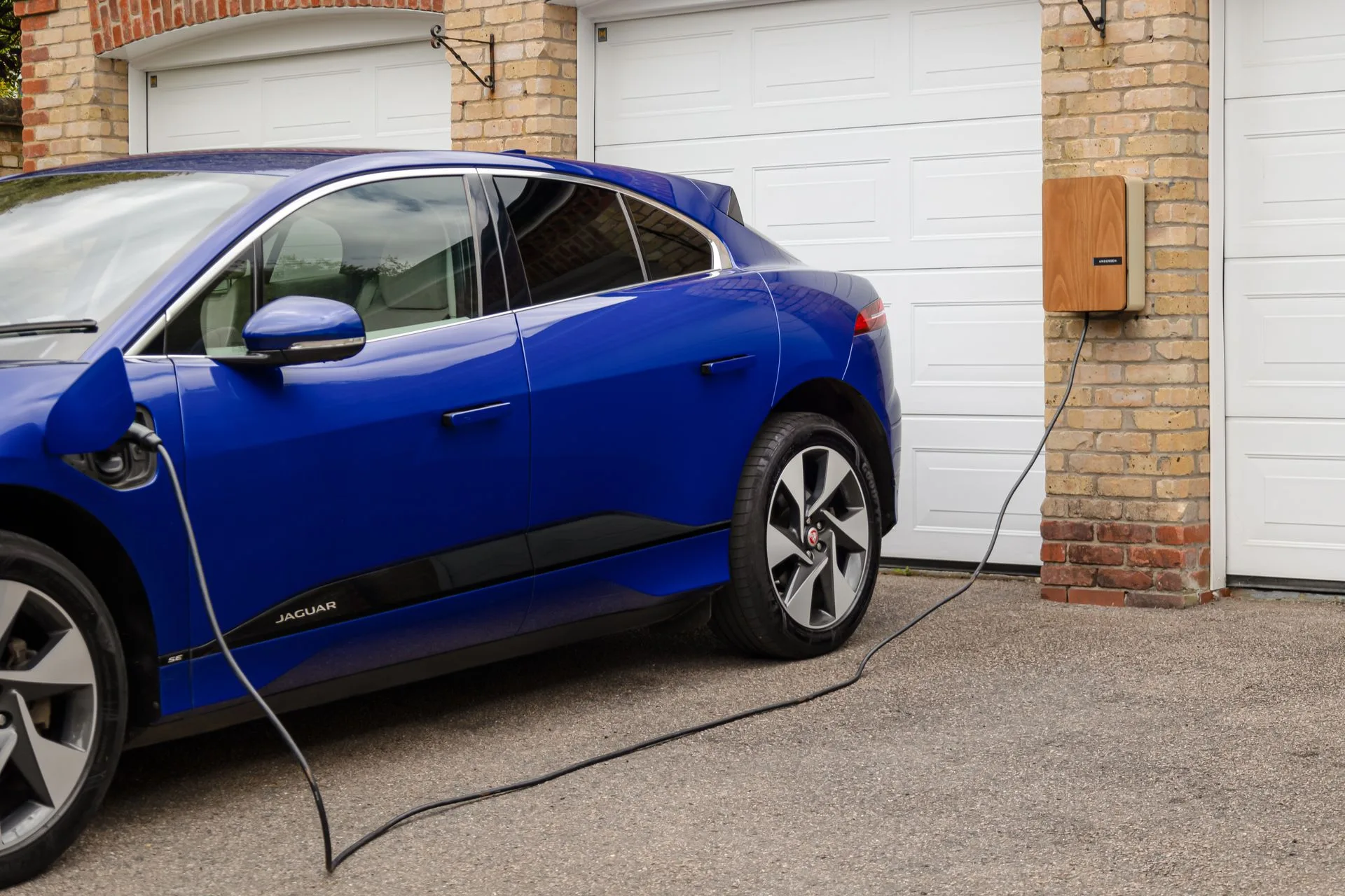 Blue electric car plugged into a wall-mounted home charger beside a garage door