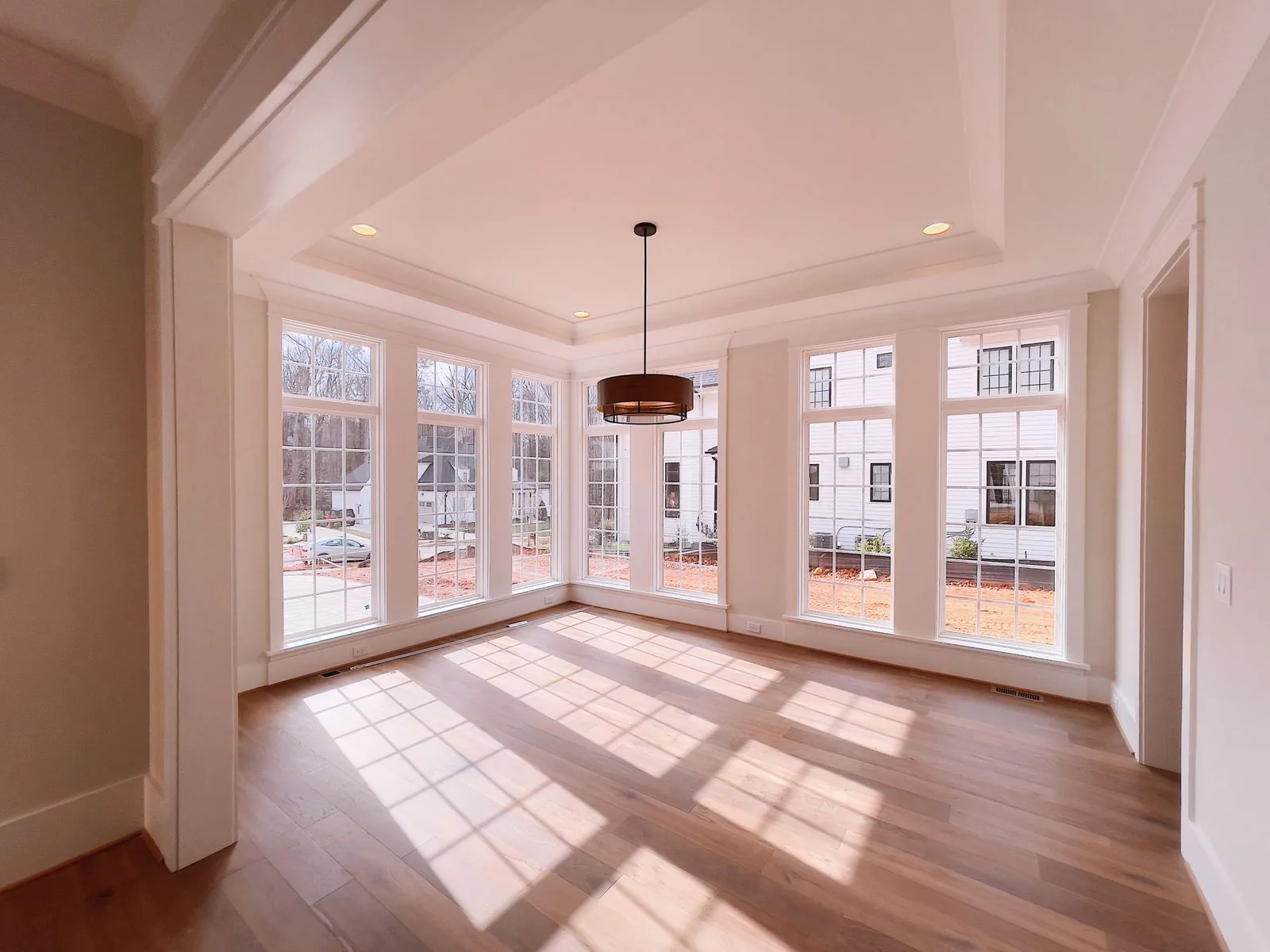 Empty room with tall bay windows casting bright patches of sunlight across a wooden floor