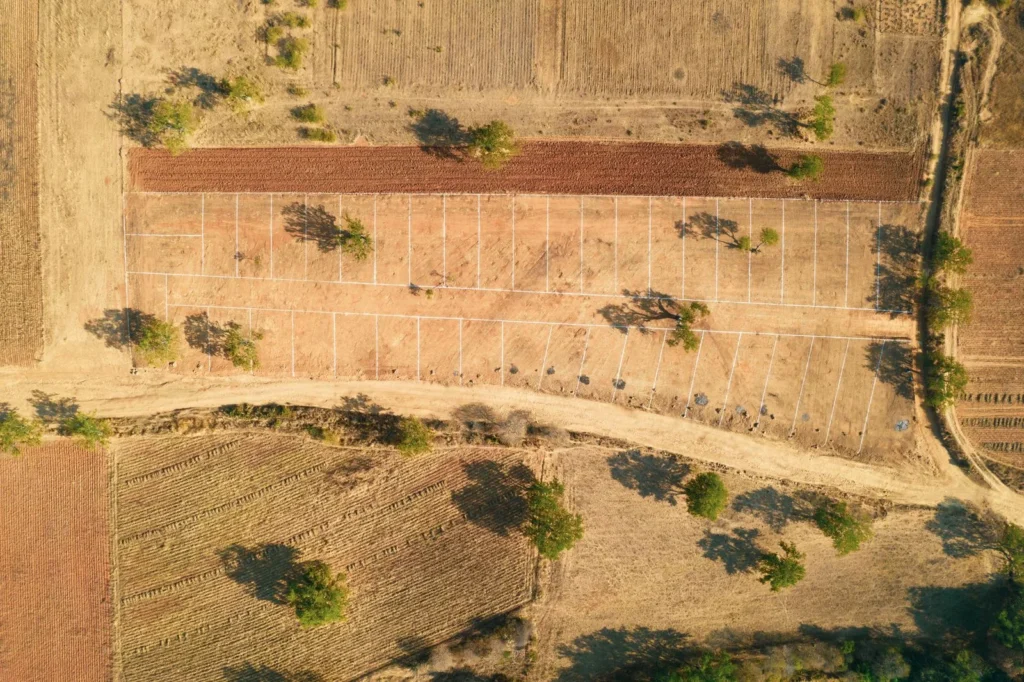 Drone view of a dry plot crossed by tracks and scattered trees, the raw ground an architectural site analysis starts from