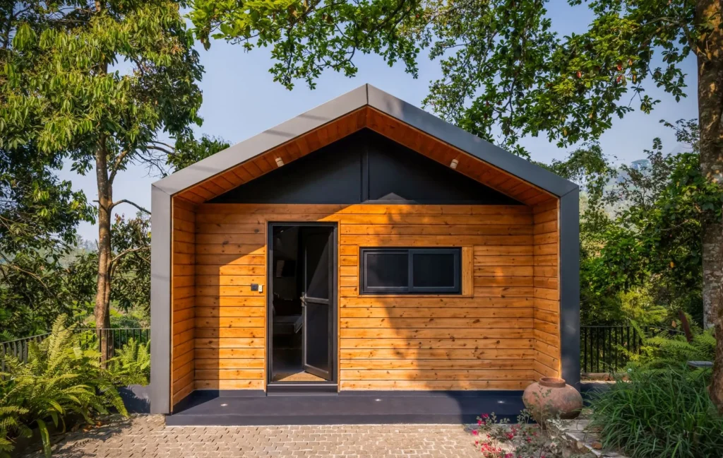 Compact timber-clad cabin with a dark gabled frame and small windows set among trees, one of many eco-friendly tiny homes built small and tight
