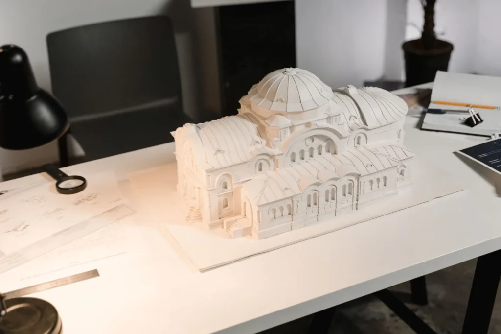 Detailed white architectural model of a domed building on a studio desk