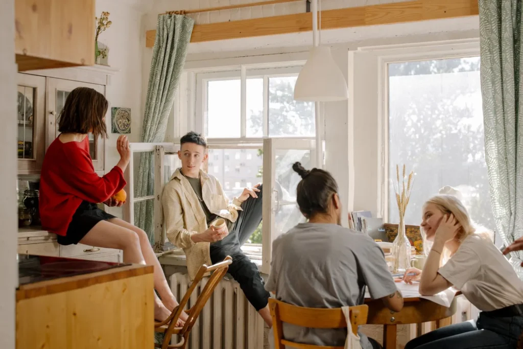 Four young roommates talking around a table in a sunny shared kitchen