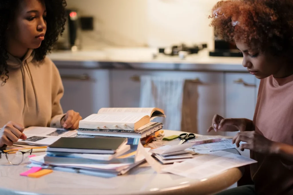 Two students working through a shared pile of books and notes at one table, a simple habit for saving money as an architecture student