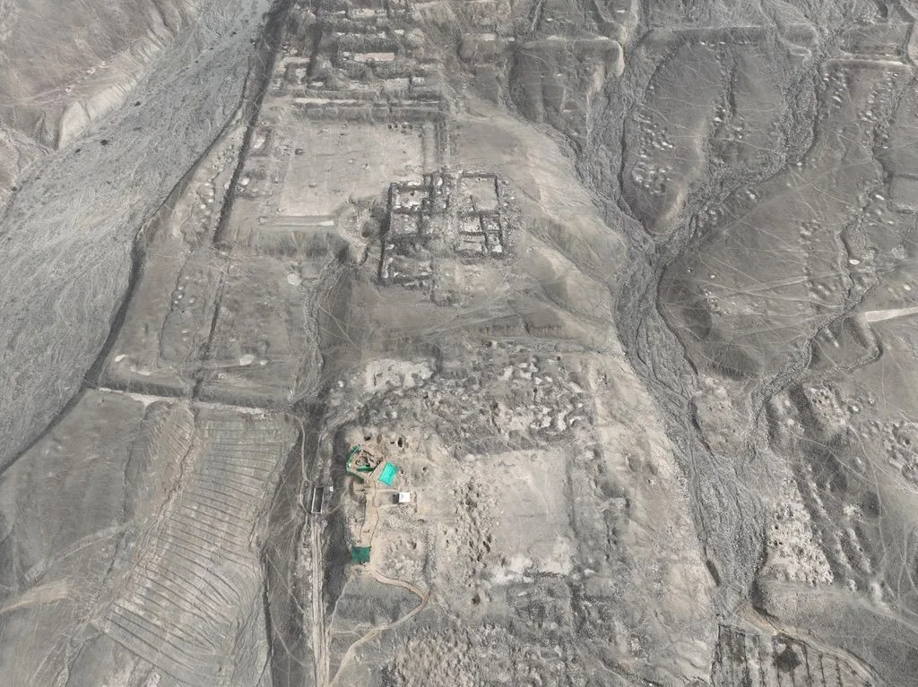 Grey aerial view of eroded adobe walls and rectangular enclosures in a dry landscape