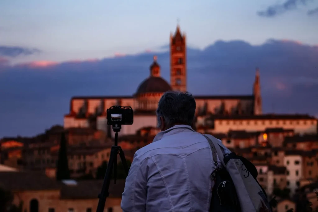 Photographer with a camera on a tripod waiting for dusk light on Siena Cathedral and the old town