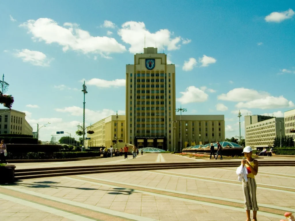 Visitors crossing a broad paved square in front of a symmetrical high rise civic building on a sunny day