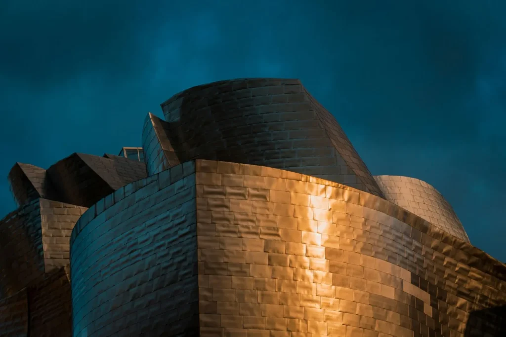 Close crop of the curving titanium cladding of the Guggenheim Museum Bilbao against a dark sky, one of the classic architectural photography examples