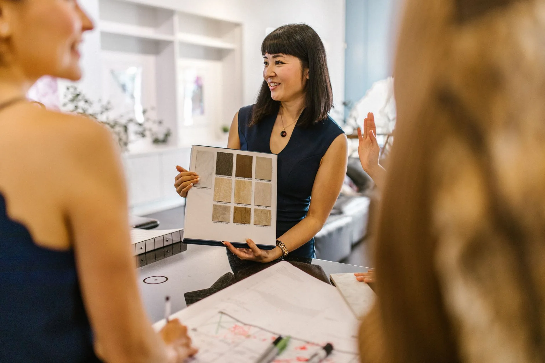 Interior designer smiling while showing a board of beige and brown flooring samples to clients across a table