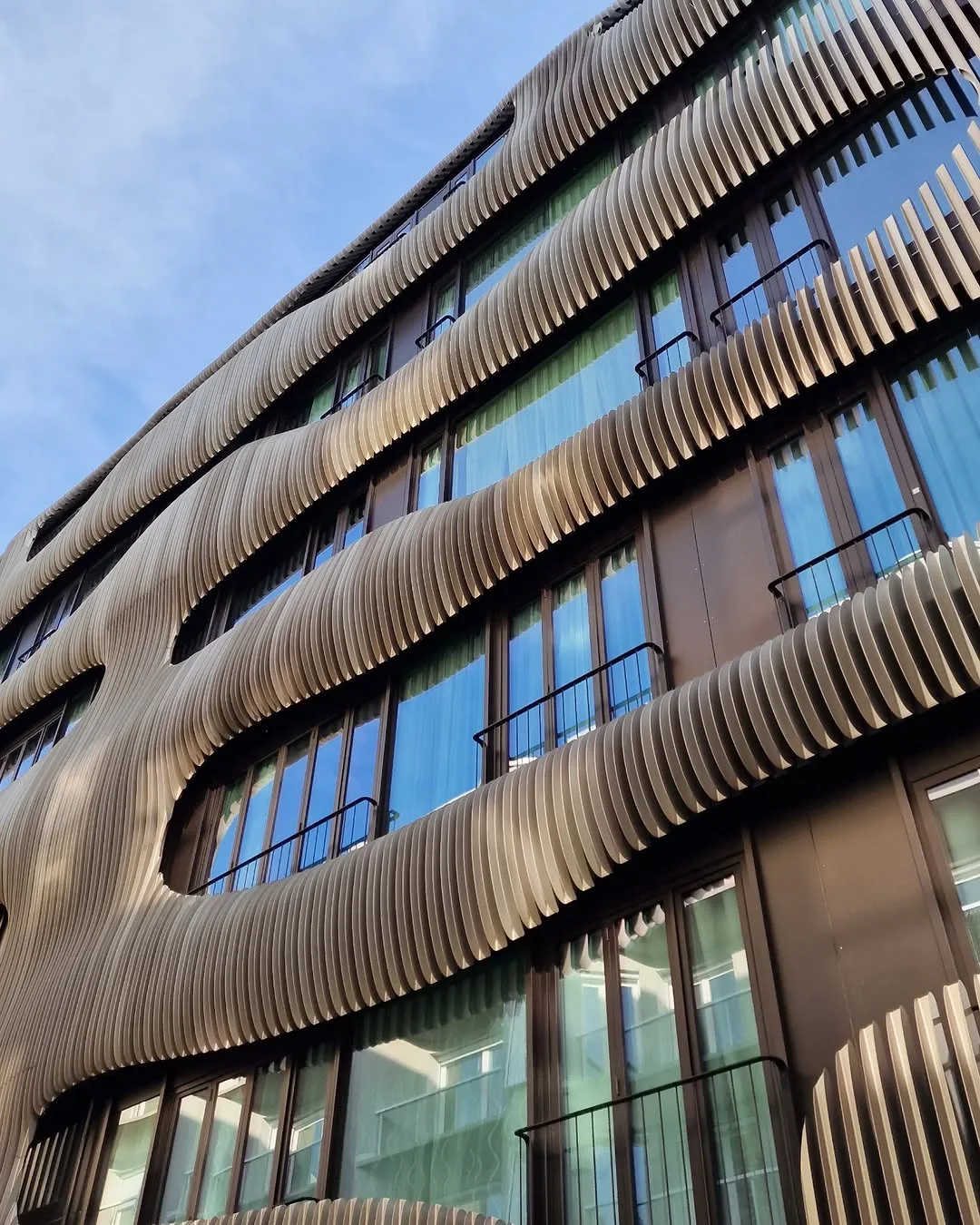 Photograph of the JOH3 facade by J. Mayer H. Architects, where wavy metal fins shift across floors to create a parametric rhythm