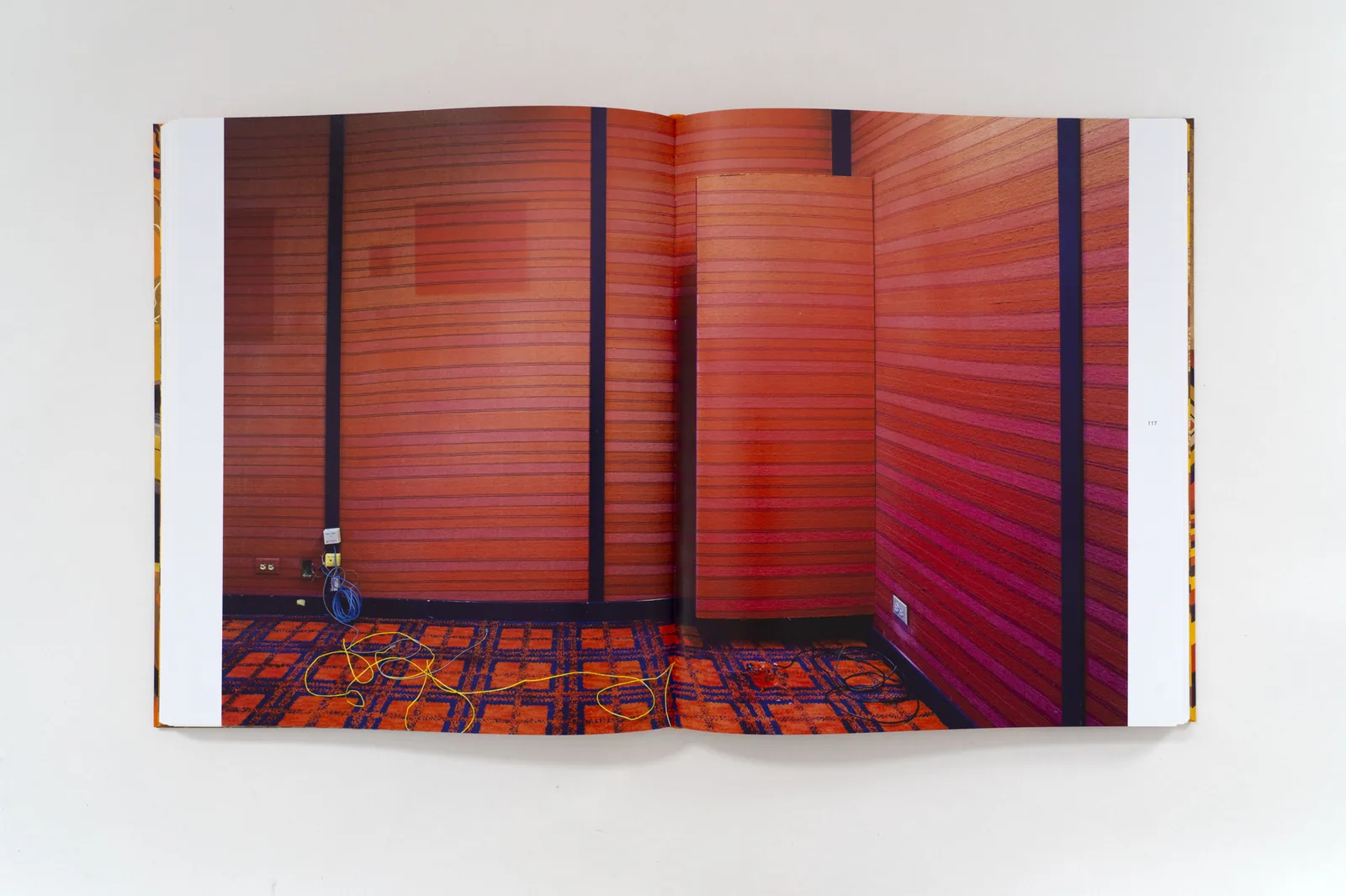 Open book spread of an empty room with full height red slatted wall panels and a red and orange patterned carpet