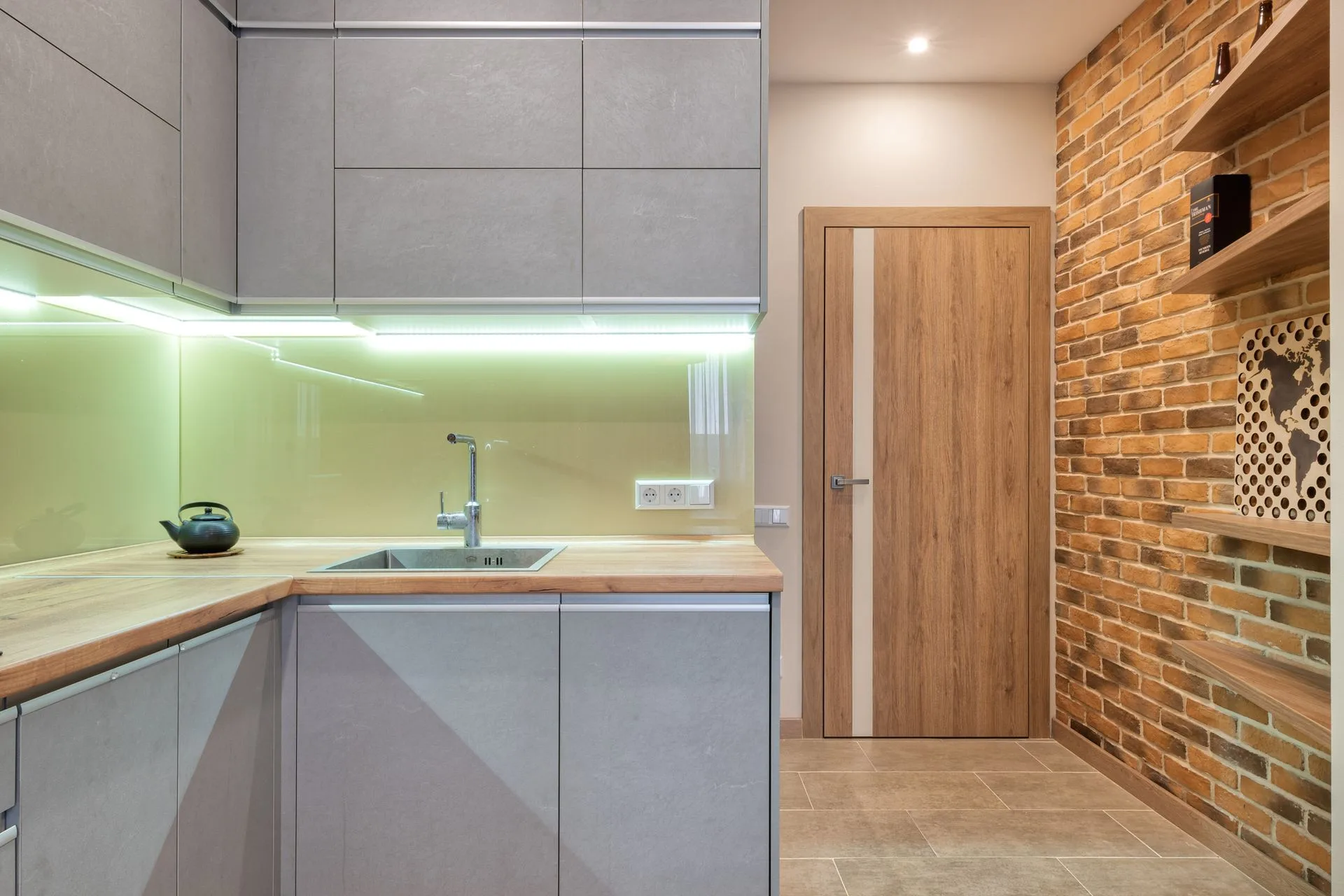 Kitchen with under-cabinet LED strip lighting over a timber worktop, a double socket on the backsplash and a brick feature wall