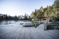 Wide timber deck with built in benches leading to the pitched roof snack bar by the lake, Lake House Völs by NOA