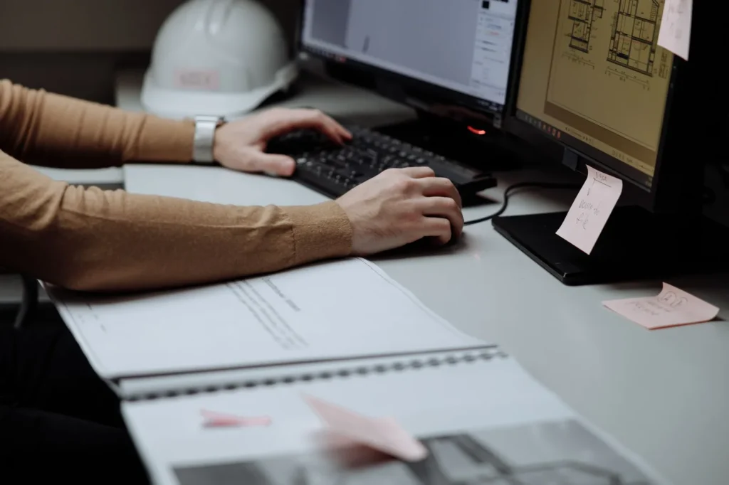 Hands on a keyboard and mouse in front of monitors showing CAD floor plans