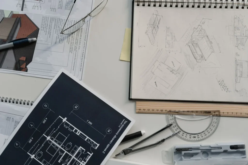 Printed plan drawings, a sketchbook and drafting tools on a desk, showing why autocad tips on layers matter for clean output