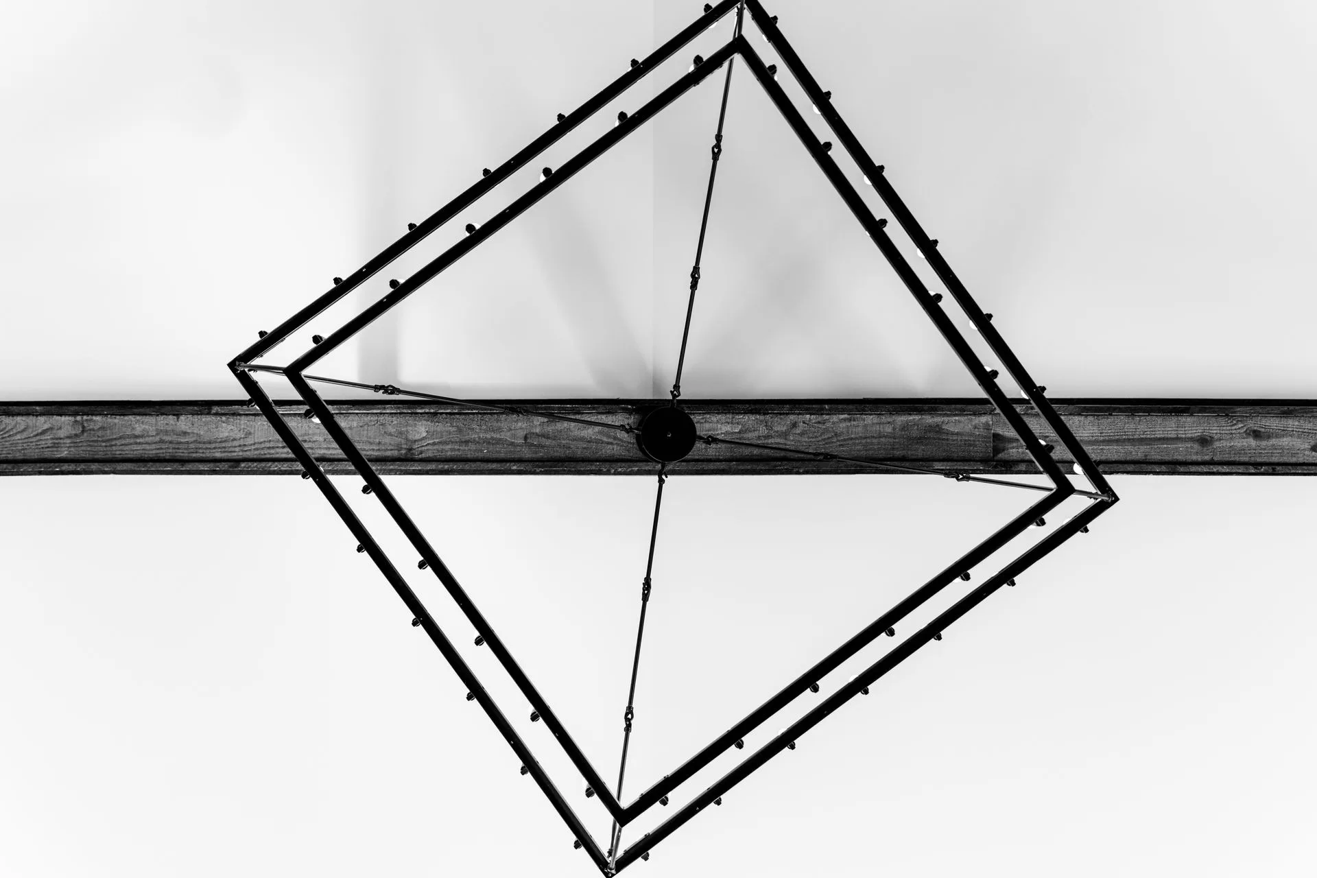 Matte black geometric chandelier with a double square frame seen from below against a white ceiling