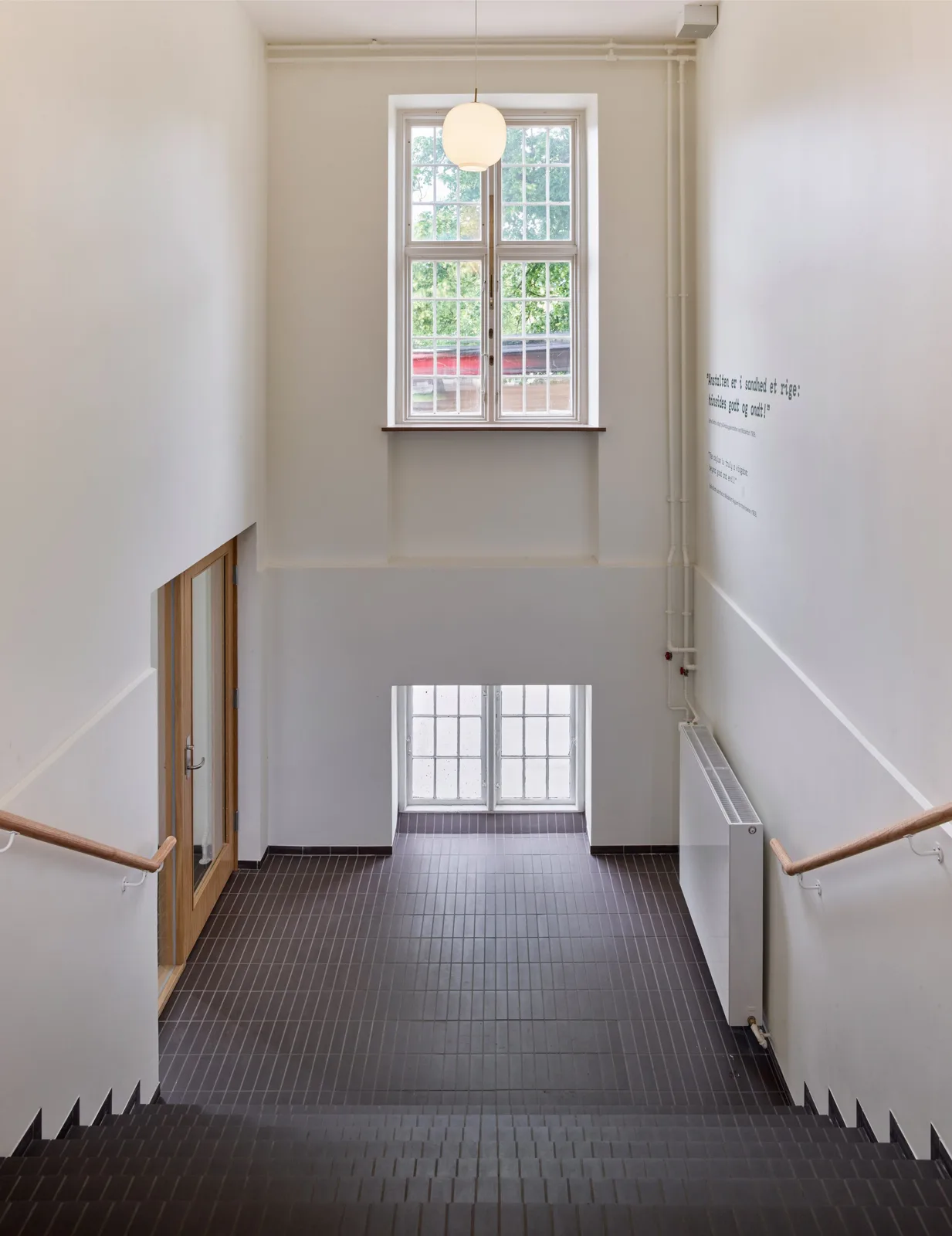 White stair hall with a tall window, pendant light and a dark floor at the reinstated entrance