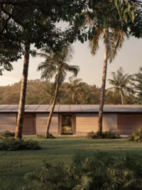 Earth toned walls under a long low metal roof among palms, with a framed opening to the garden, Monsoon by YODEZEEN