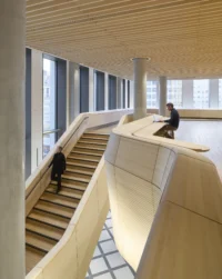 Sculpted double curved timber stair and balustrade in the D-block with a person walking down, New Government Quarter by Nordic Office of Architecture