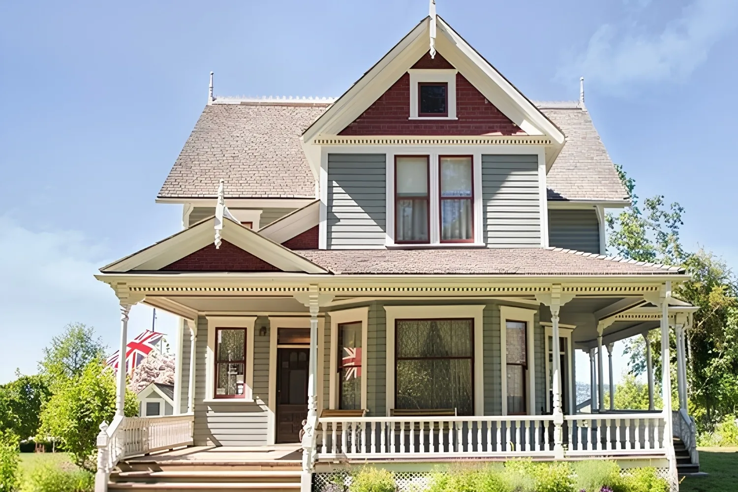 Victorian house with gabled roofs, grey siding and a white wraparound porch