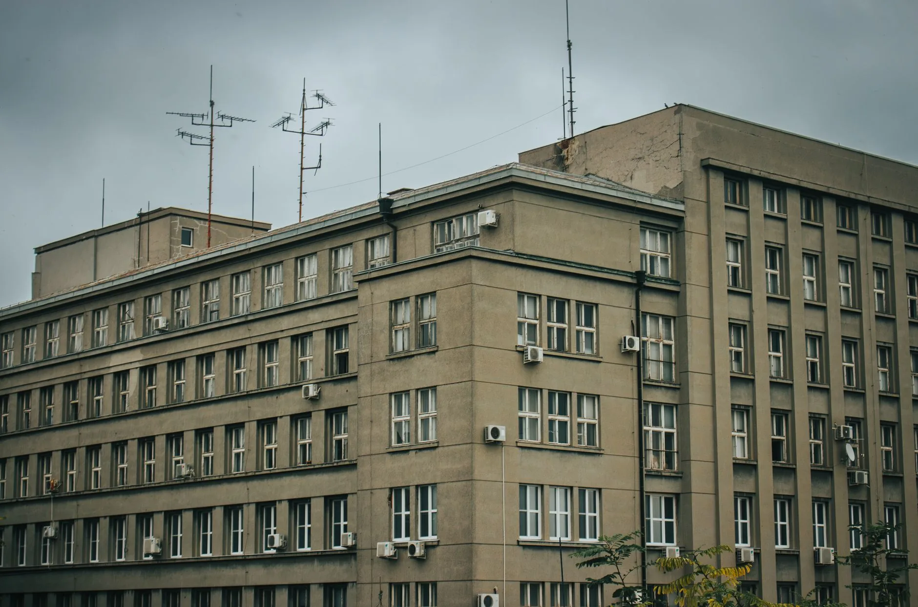 Weathered mid-century office block with rows of windows, air conditioning units and rooftop antennas under a grey sky
