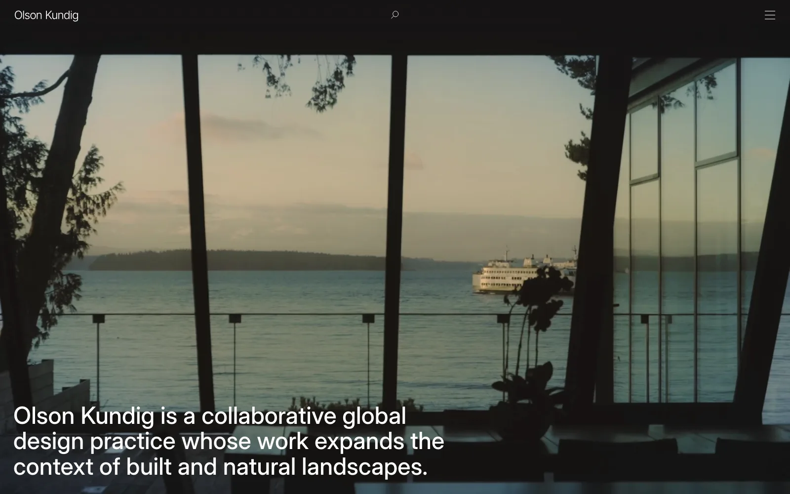 Olson Kundig homepage opening on a dark interior view through tall windows toward water and a ferry