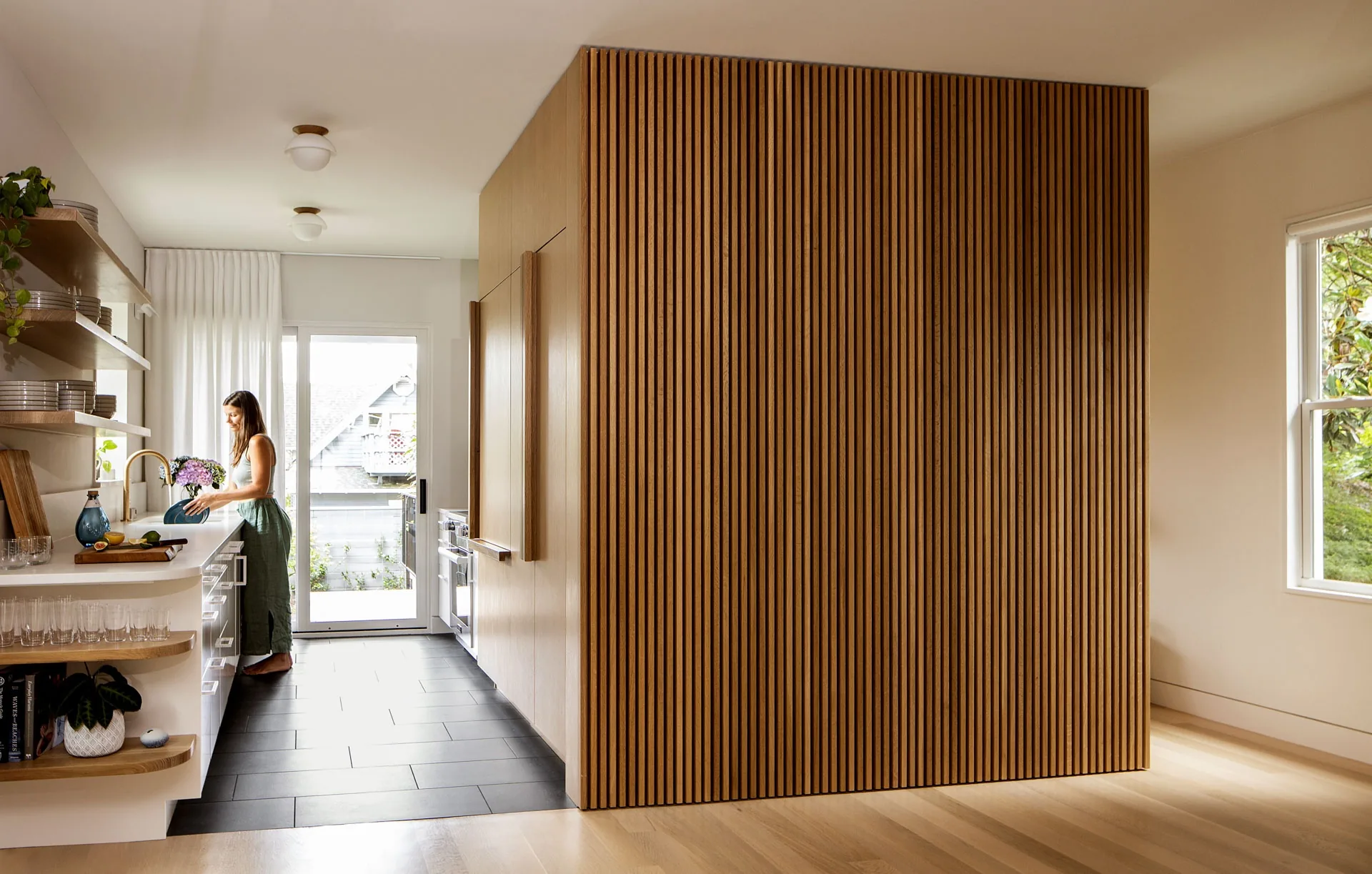Kitchen running past a box clad in vertical white oak battens that hides the pantry and refrigerator, Phinney Mini by Best Practice Architecture