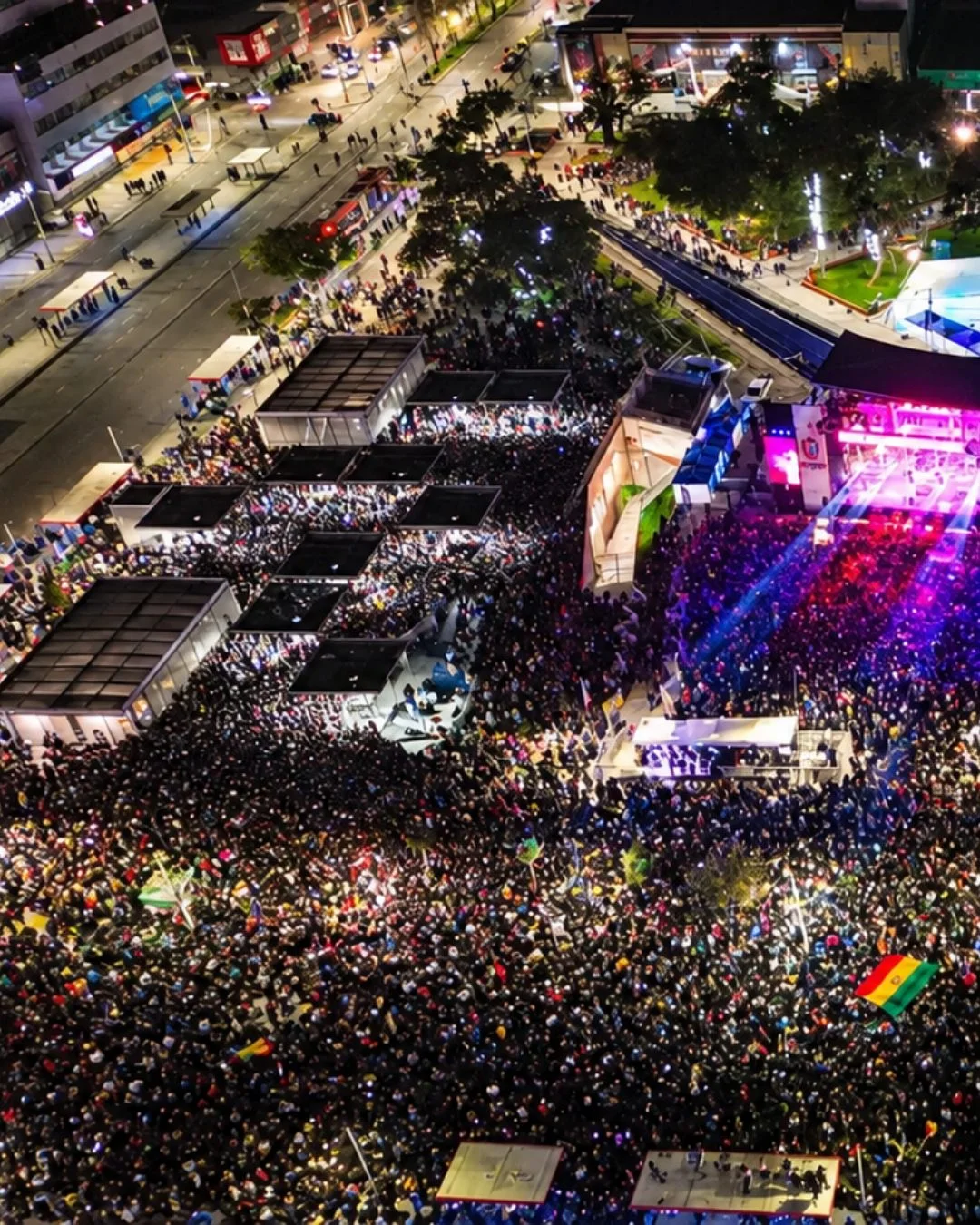 Aerial photo of a dense crowd filling an urban plaza during a nighttime event with stage lighting