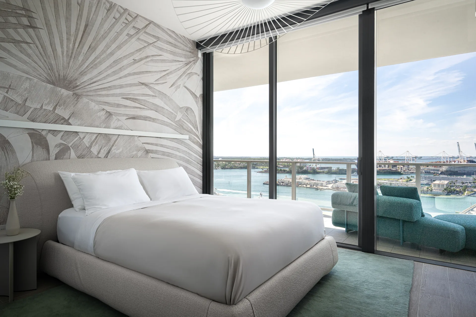 Guest bedroom with an oversized palm leaf mural behind the bed and a green rug by the bay view windows, PS Apartment by Nar Design Studio