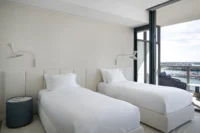 Second guest bedroom with twin beds under a wall to wall upholstered headboard and wall lamps, PS Apartment by Nar Design Studio