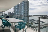 Terrace dining table with aqua woven chairs overlooking the Miami Beach Marina and towers, PS Apartment by Nar Design Studio