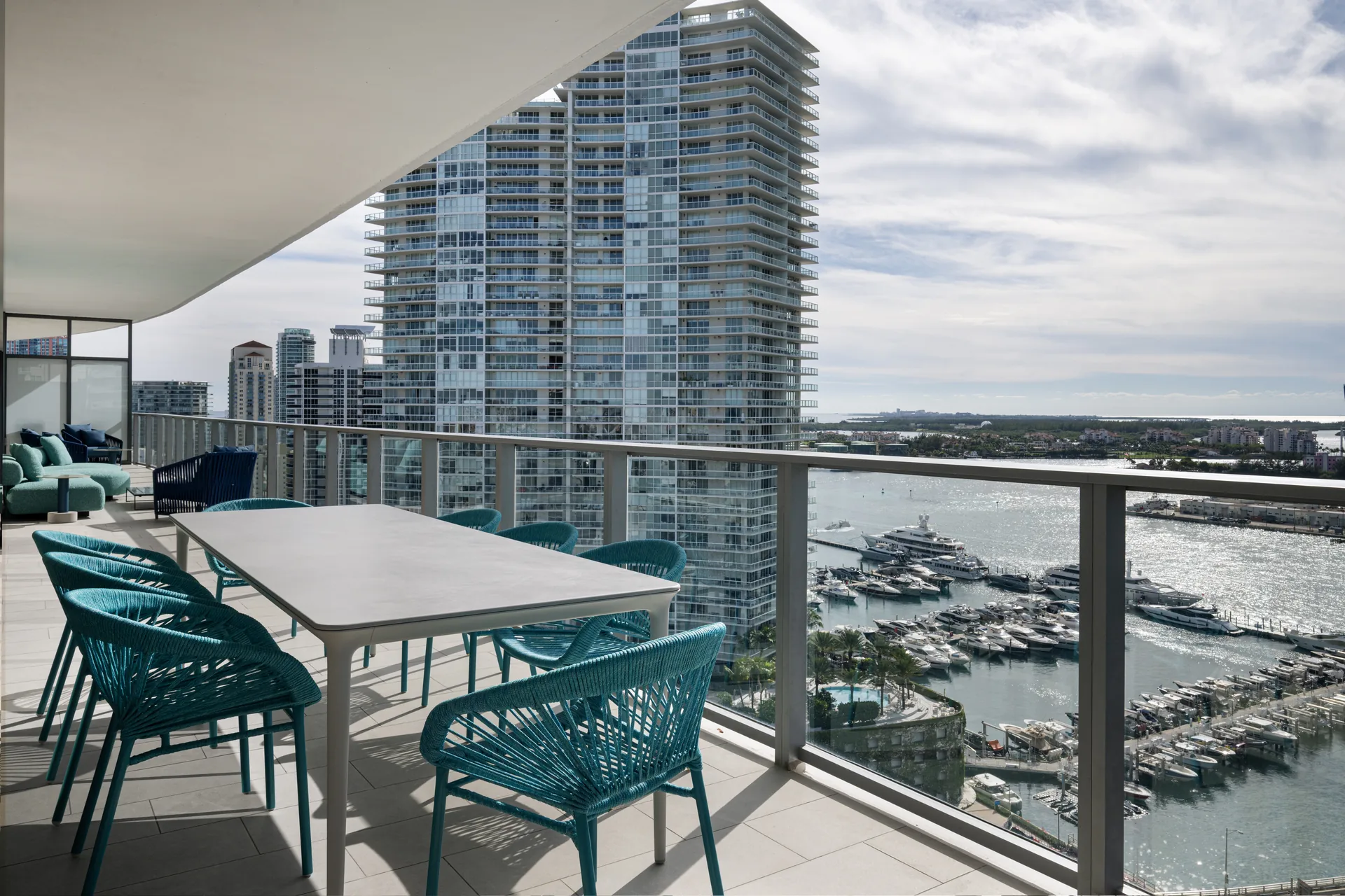 Terrace dining table with aqua woven chairs overlooking the Miami Beach Marina and towers, PS Apartment by Nar Design Studio