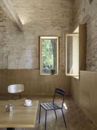 Corner of a brick room with oak wainscot, an open casement window, a teapot on a table and two chairs
