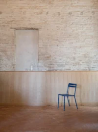 Bare brick wall with a filled-in former doorway above oak wainscot and a single blue chair