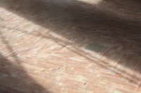 Close view of hand-molded terracotta tiles laid in a herringbone pattern catching low sunlight