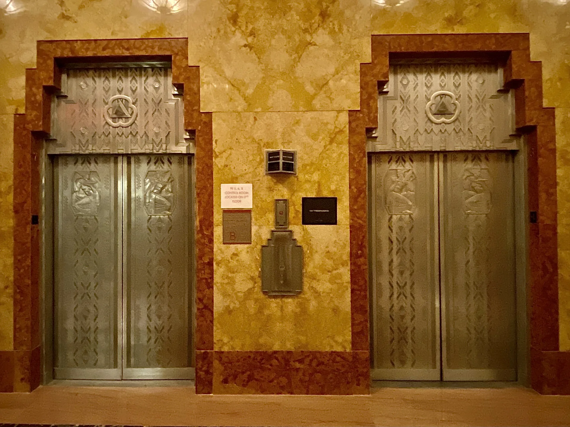 Art Deco elevator doors with stepped marble frames and etched metal panels in the 70 Pine Street lobby