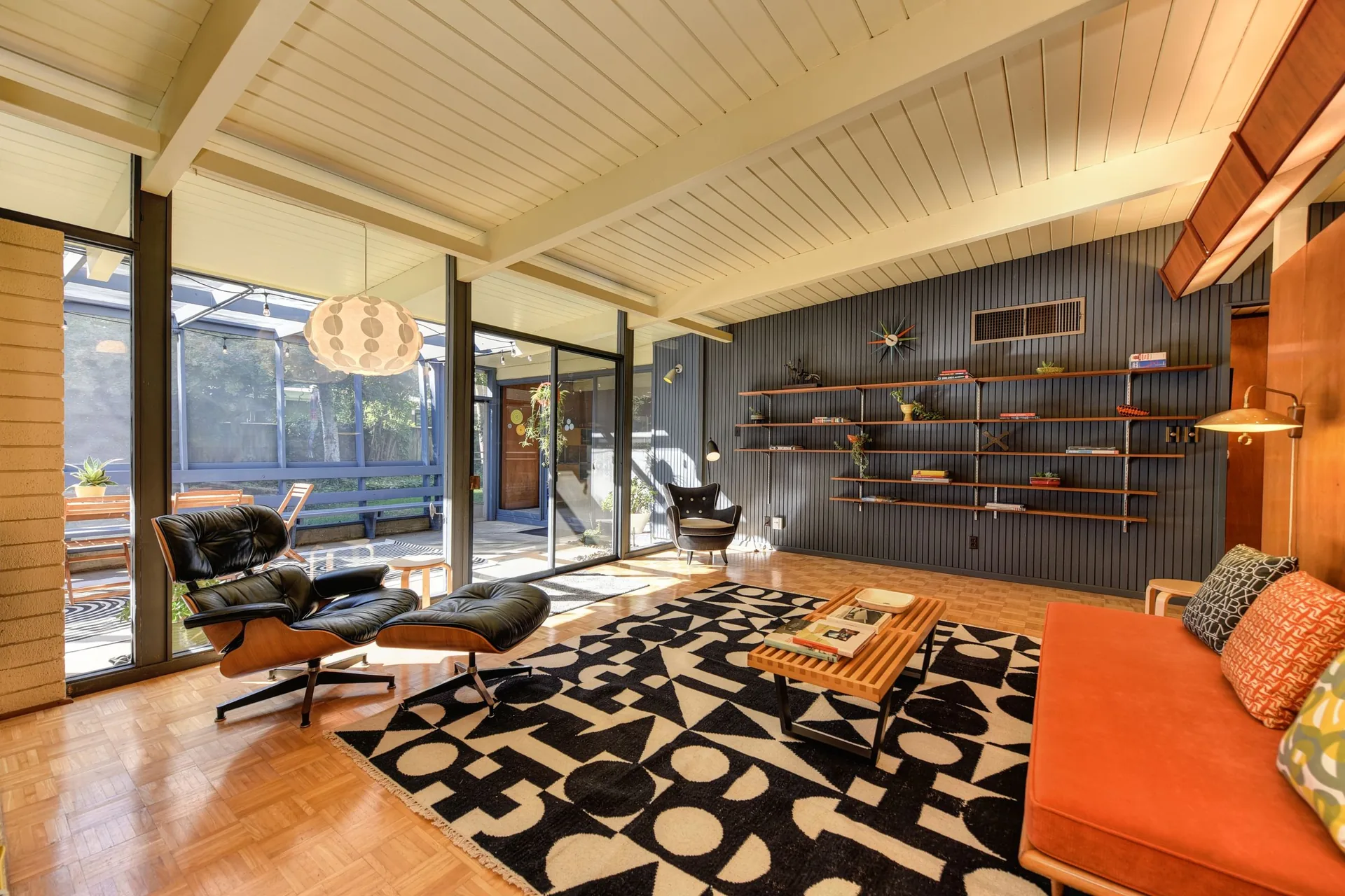Mid-century modern living room with a leather lounge chair, orange sofa, wall shelving and a bold graphic rug