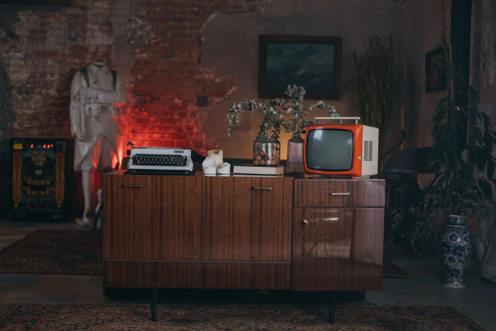 Polished vintage sideboard on tapered legs topped with an orange portable TV and a typewriter