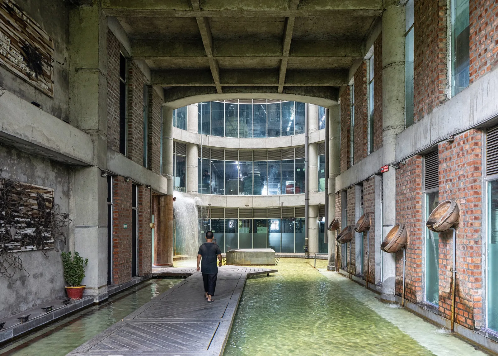 Long internal courtyard with a shallow water channel, brick walls, hanging lanterns and a glazed atrium at the far end