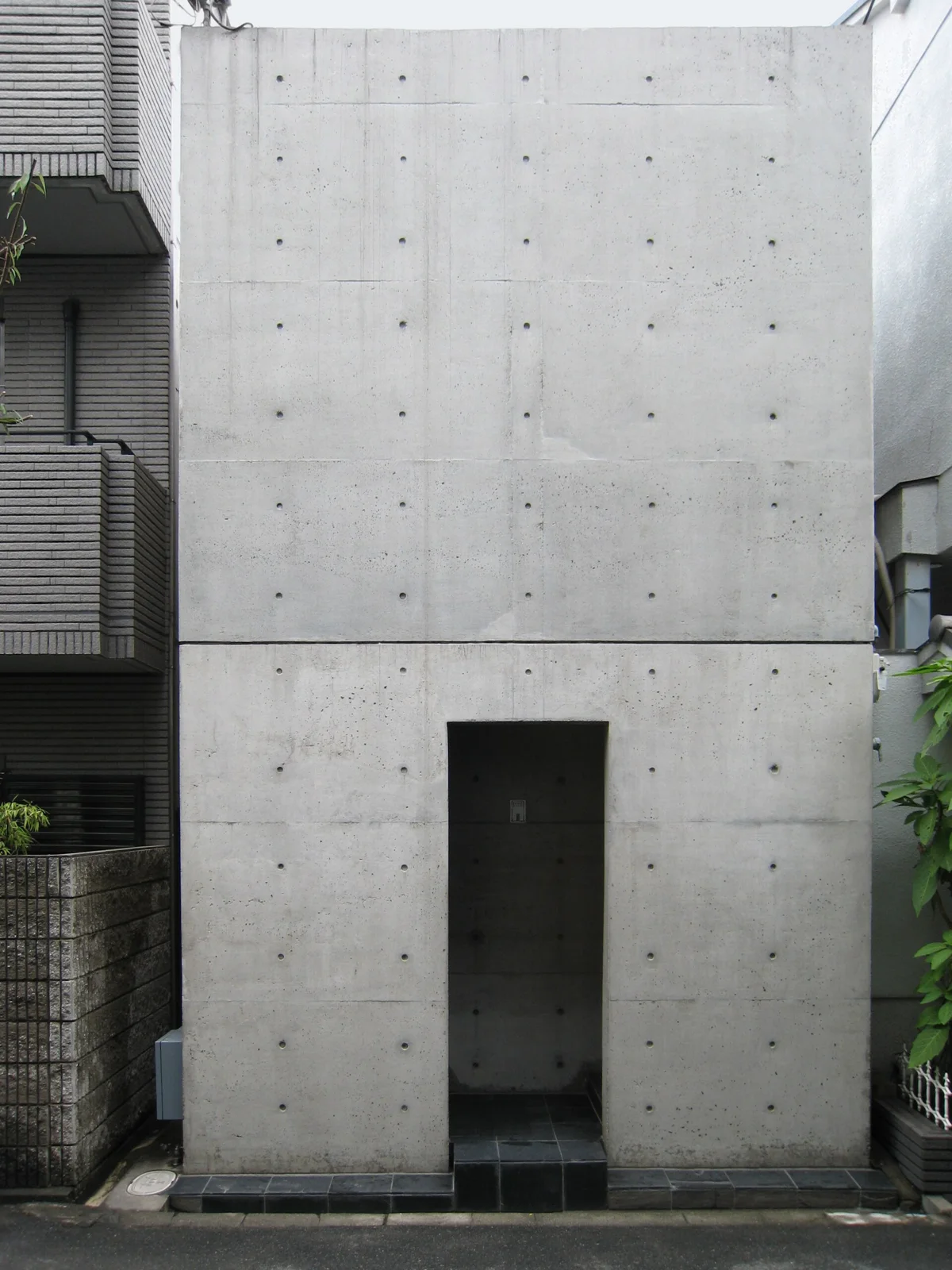 Street front of Tadao Ando Row House in Sumiyoshi, a plain concrete plane with one recessed entrance and no ornament