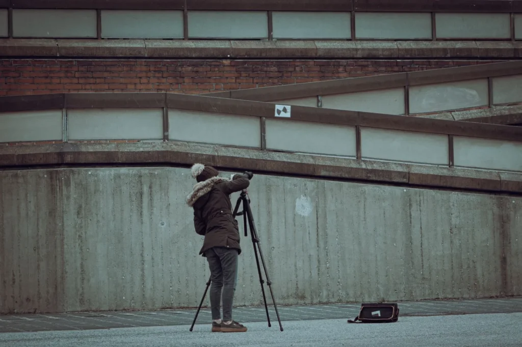 Photographer in winter clothes shooting a concrete building with a camera on a tripod